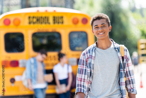 Photography happy teen african american schoolboy looking at camera in front of school bus