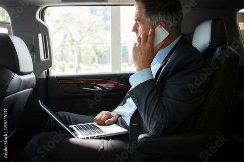 Papier peint Handsome businessman talking with phone sitting with laptop on the backseat of the car