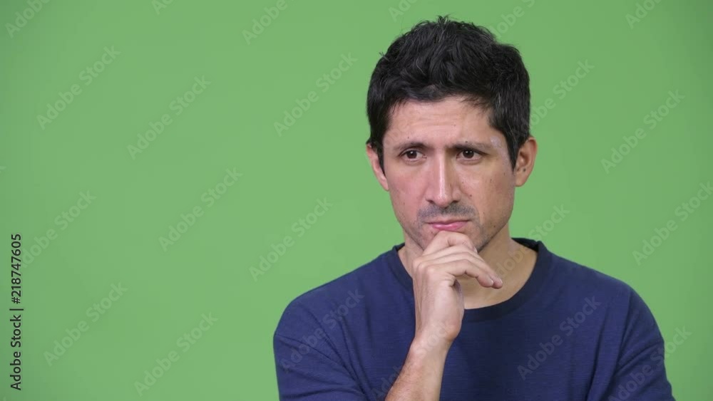Serious Hispanic man thinking against green background Serious Hispanic man thinking against green background