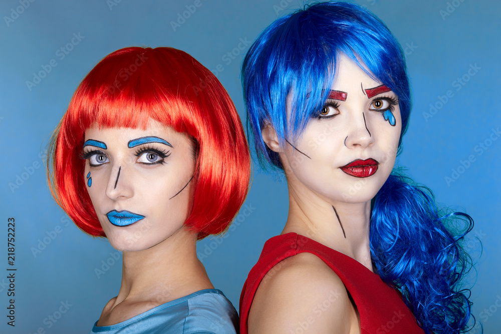 Obraz premium Portrait of young women in comic pop art make-up style. Females in red and blue wigs on blue background