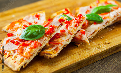 sliced Pizza with Mozzarella cheese, Ham, Tomatoes, pepper, Spices and Fresh Basil. Italian pizza on wooden background.