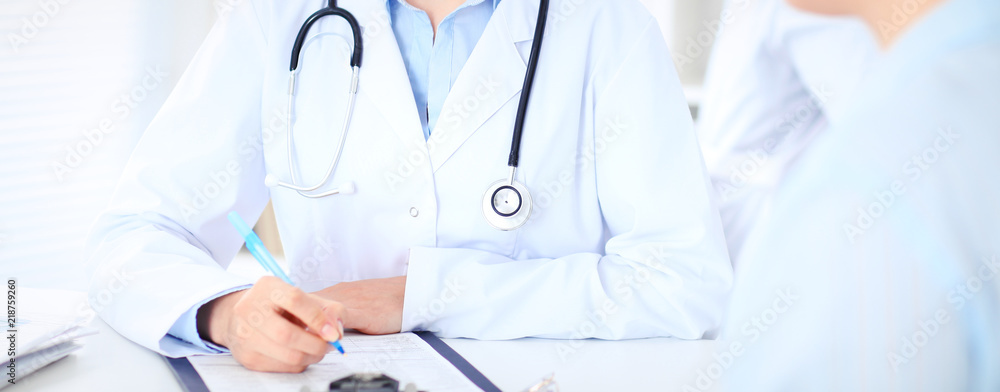 Unknown female doctor and patient discussing something while sitting at the table at hospital. Medicine and healthcare concepts Unknown female doctor and patient discussing something while sitting at the table at hospital. Medicine and healthcare concepts