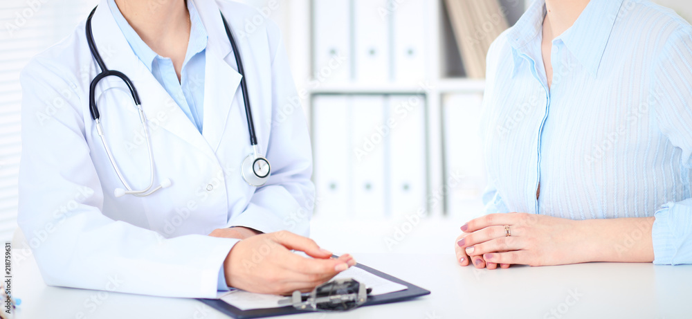 Unknown female doctor and patient discussing something while sitting at the table at hospital. Medicine and healthcare concepts Unknown female doctor and patient discussing something while sitting at the table at hospital. Medicine and healthcare concepts