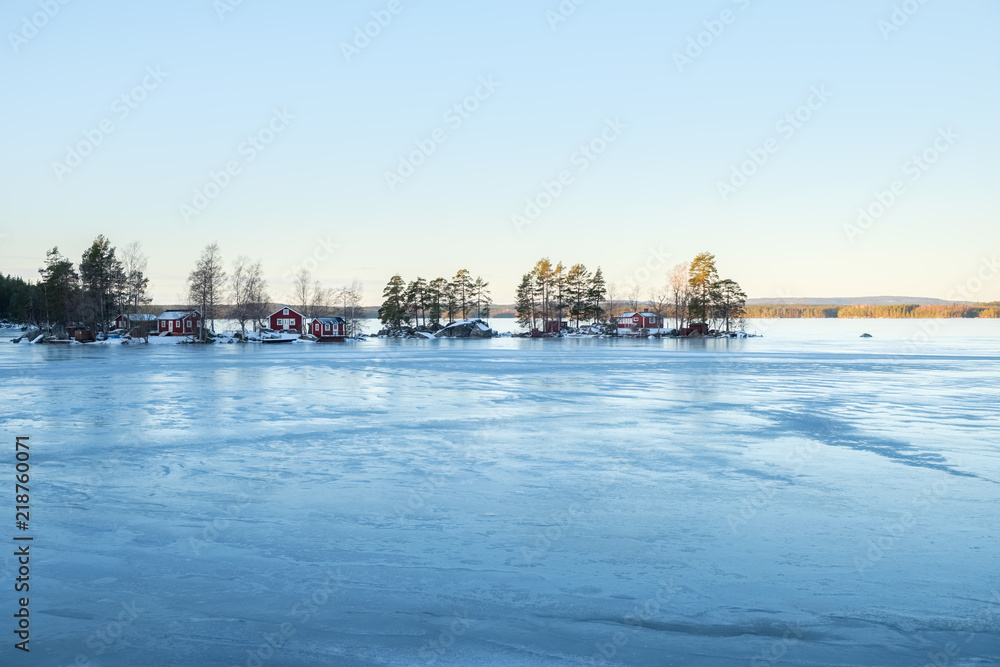 Winter landscape with red wooden house on a lake in Sweden.