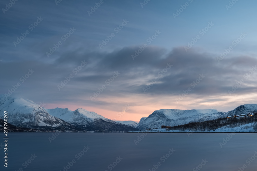 Landscape of a Norwegian fjord and town in winter at sunset.