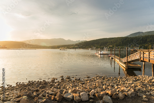 Scenic Bay at Sunset with a Wooden Pier and a Rochy Shore in Foreground. Port Moody, BC, Canada. © alpegor