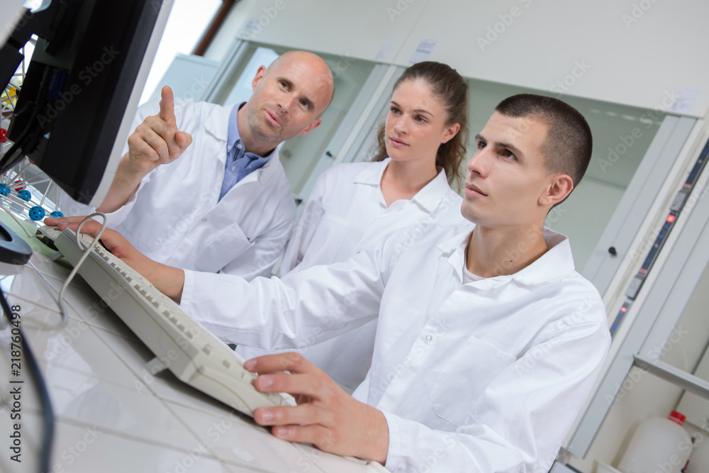 Students and teacher in labcoats loking at computer Students and teacher in labcoats loking at computer