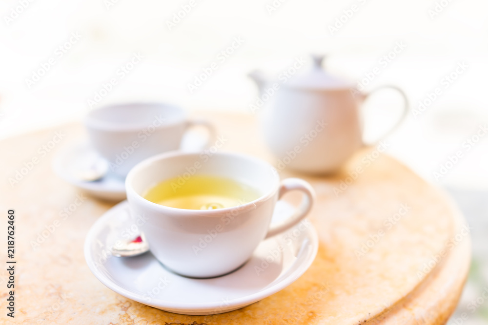 Closeup of two white cups on plates of green or oolong tea in breakfast brunch outdoor cafe restaurant outside wooden table with sunny colorful sunlight, teapot, pot