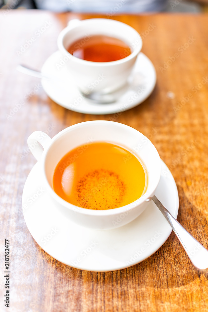 Closeup of two white cups on plates of green or oolong tea in breakfast brunch outdoor cafe restaurant outside wooden table with orange colorful vibrant saturated color Closeup of two white cups on plates of green or oolong tea in breakfast brunch outdoor cafe restaurant outside wooden table with orange colorful vibrant saturated color