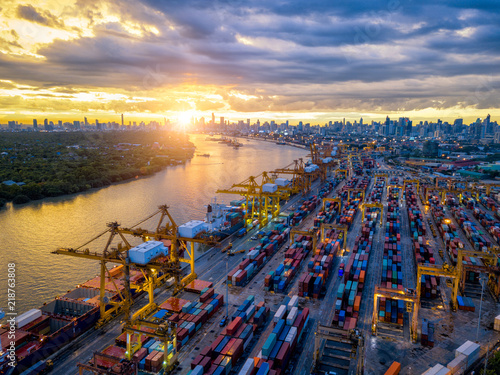 Aerial view of international port with Crane loading containers in import export business logistics with cityscape of Bangkok city Thailand at sunset