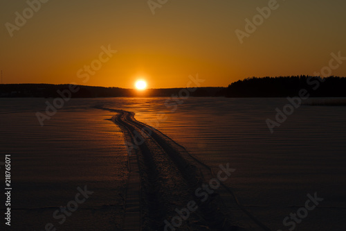 Finnish winter landscape with yellow sunset. In the snow going to the horizon snowmobile trail.