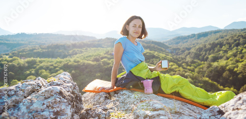 A woman is drinking coffee while sitting on top of a mountain.