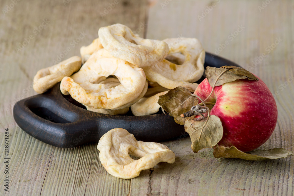 Fototapeta premium Dessert. Dried apple rings on a round wooden plate, next to a ripe apple on an old wooden table.