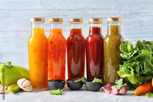 Bottles with different tasty sauces and vegetables on light table photo