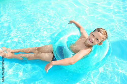 Cute little boy with inflatable ring swimming in pool