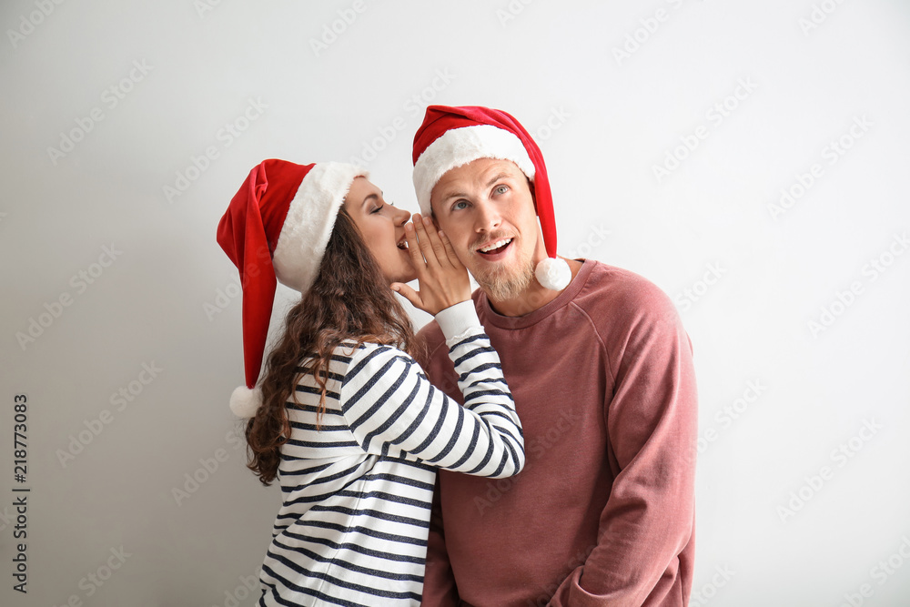 Obraz premium Portrait of cute young woman in Santa hat telling secret to her boyfriend on white background