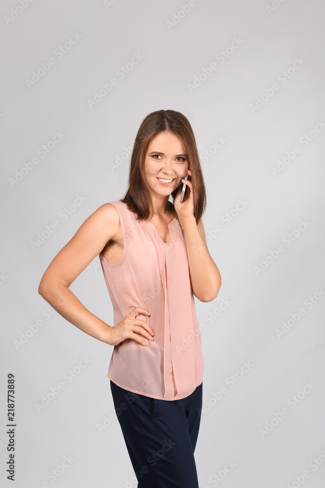 Young businesswoman talking by mobile phone on grey background Young businesswoman talking by mobile phone on grey background