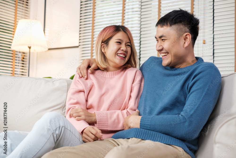 Asian couple embracing and laughing while sitting at sofa in house.lover couple in home concept.