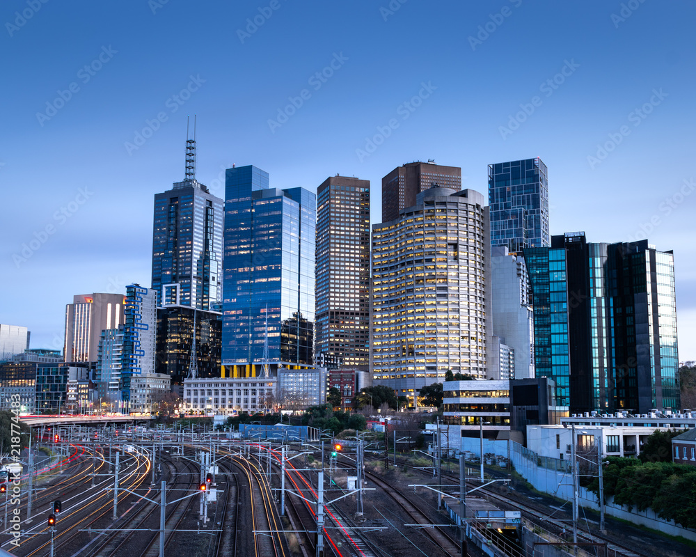 Obraz premium Lekkie szlaki na torach kolejowych prowadzą nas w stronę panoramę Melbourne.