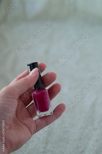 pink nail polish bottle in woman's hand on the green background