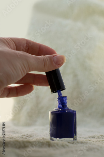 girl's hand open one small deep blue nail polish bottle which standing on the green background