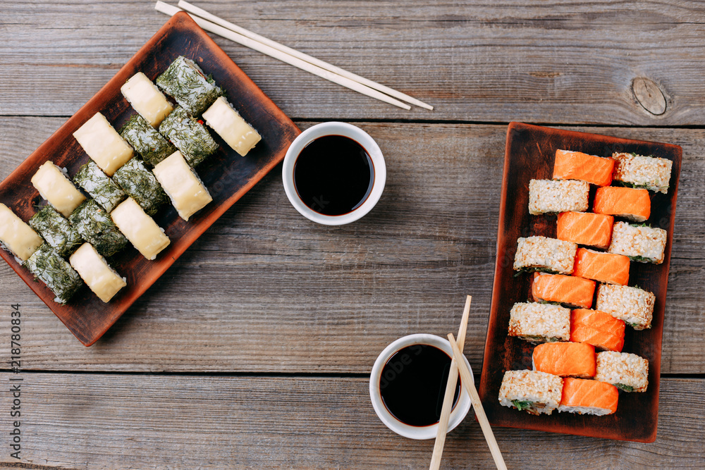 Japanese restaurant, traditional cuisine. Appetizing set of sushi rolls served on clay and wooden trays, chopsticks and sauce bowls, flat lay with free space for text design Japanese restaurant, traditional cuisine. Appetizing set of sushi rolls served on clay and wooden trays, chopsticks and sauce bowls, flat lay with free space for text design