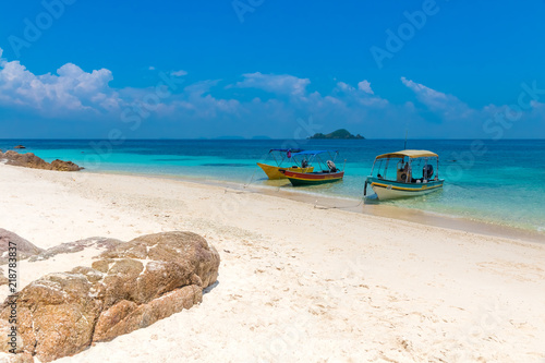 Three tourist boats anchoring on a white powdery sandy beach, a blue sky and a small island on the horizon makes it a gorgeous scene of the uninhabited Rawa Island near Perhentian Kecil in Malaysia. photo