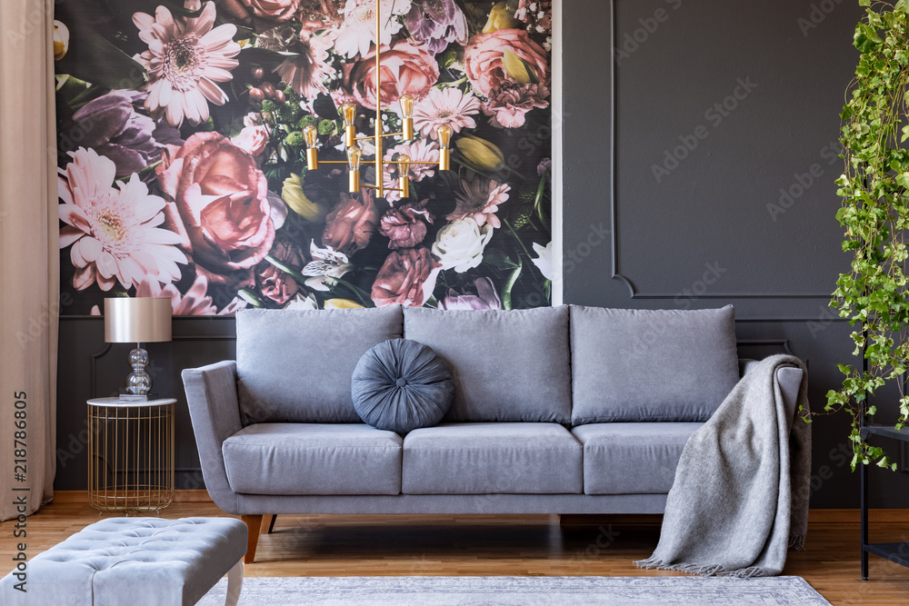 Cushion and blanket on a stylish sofa in a gray living room interior with ivy plant and flowers print on the wall - obrazy, fototapety, plakaty 