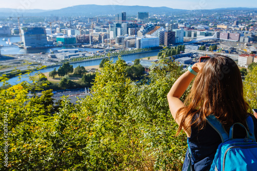 Young woman standing on the view point of Oslo and enjoying the panorama of the city. Beautiful and soft sunlight. Norway.