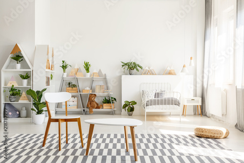 White wooden chair and table set, green plants in a spacious, sunlit teenager bedroom interior with scandinavian decor