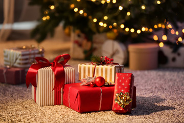 Beautiful Christmas gift boxes on floor near fir tree in room