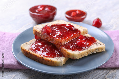 Plate with slices of bread and delicious strawberry jam on light wooden table, closeup