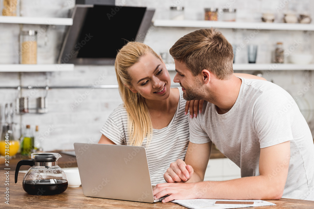 smiling couple working together with laptop in morning and looking at each other smiling couple working together with laptop in morning and looking at each other