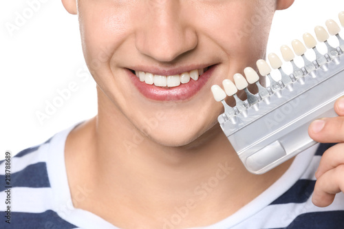 Young man with teeth color samples on white background, closeup