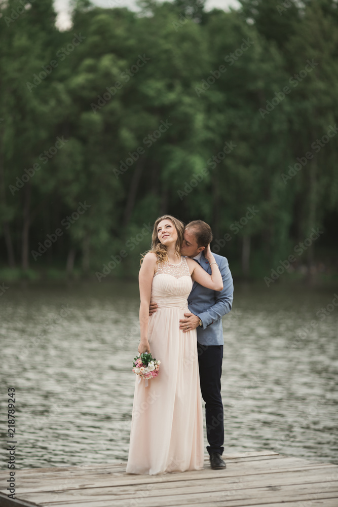 Beautiful wedding couple, bride,groom kissing and posing on the bridge near lake Beautiful wedding couple, bride,groom kissing and posing on the bridge near lake