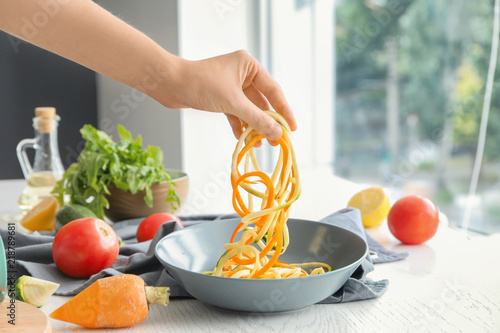 Woman holding fresh zucchini and carrot spaghetti over bowl photo
