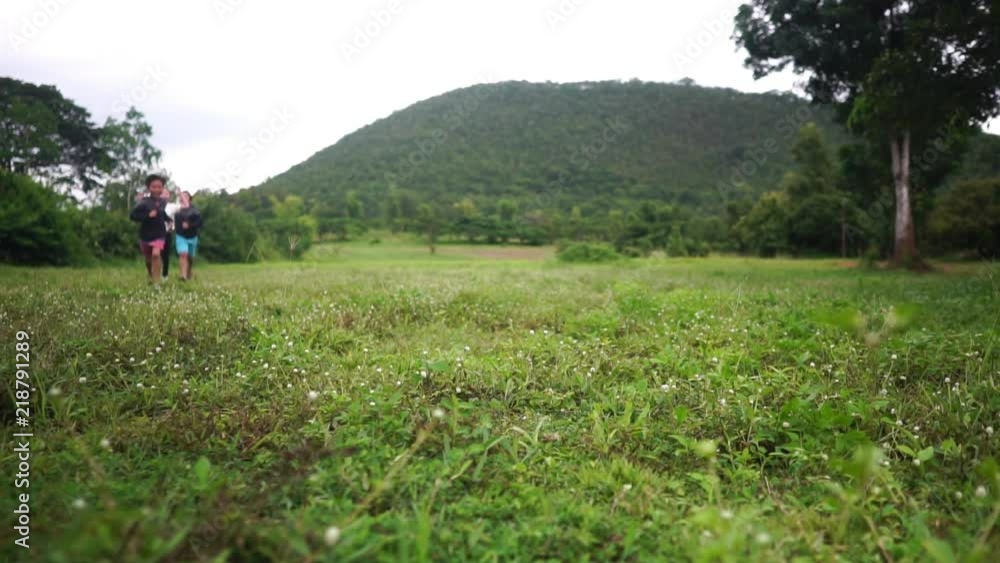 Slow motion of young Asian kids run on a green field near a hill in summer day Slow motion of young Asian kids run on a green field near a hill in summer day