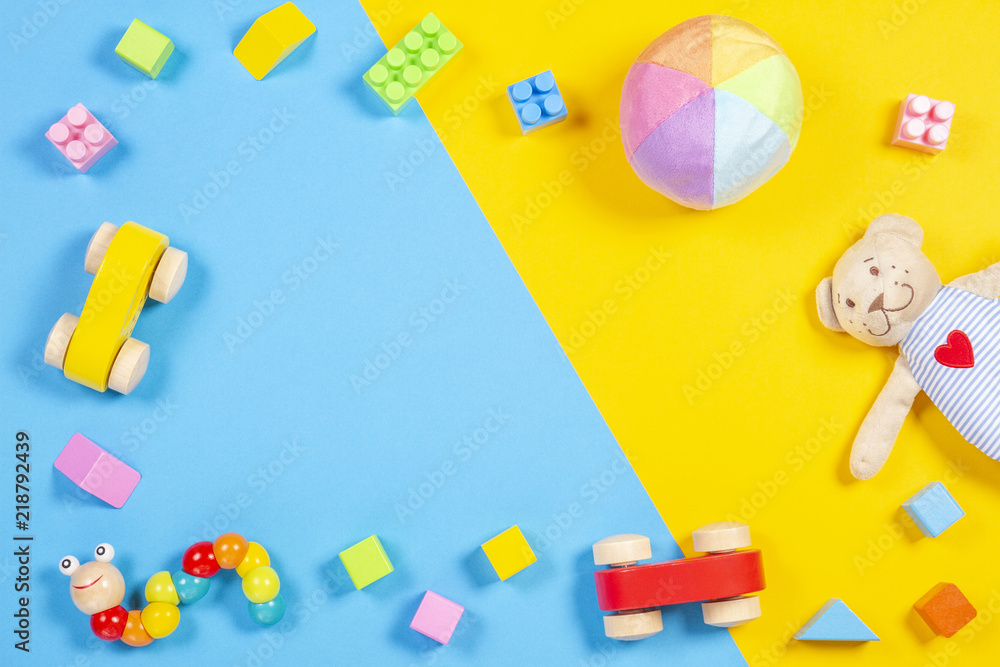 Obraz premium Baby kids toys frame with teddy bear, wooden toy car, colorful bricks on blue and yellow background. Top view