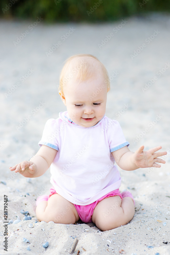 Kids lifestyle outdoor. Happy cute girl in bikini and panama playing with sand on the beach of sea. Summer vacation and family travel concept. Little baby girl sitting on the sand near the sea Kids lifestyle outdoor. Happy cute girl in bikini and panama playing with sand on the beach of sea. Summer vacation and family travel concept. Little baby girl sitting on the sand near the sea
