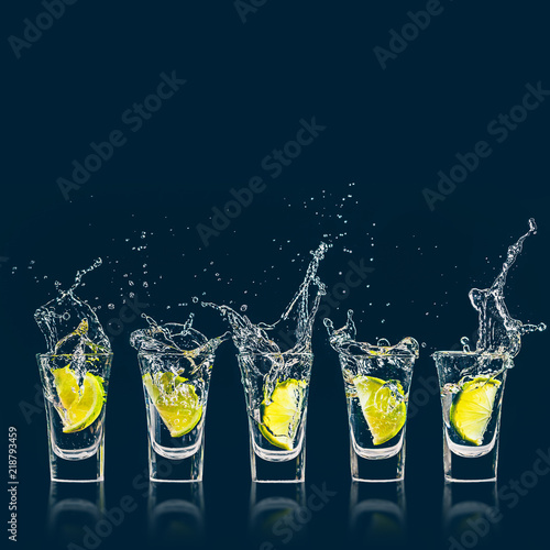 A piece of lime falls with a splash in a shot glass of vodka photo