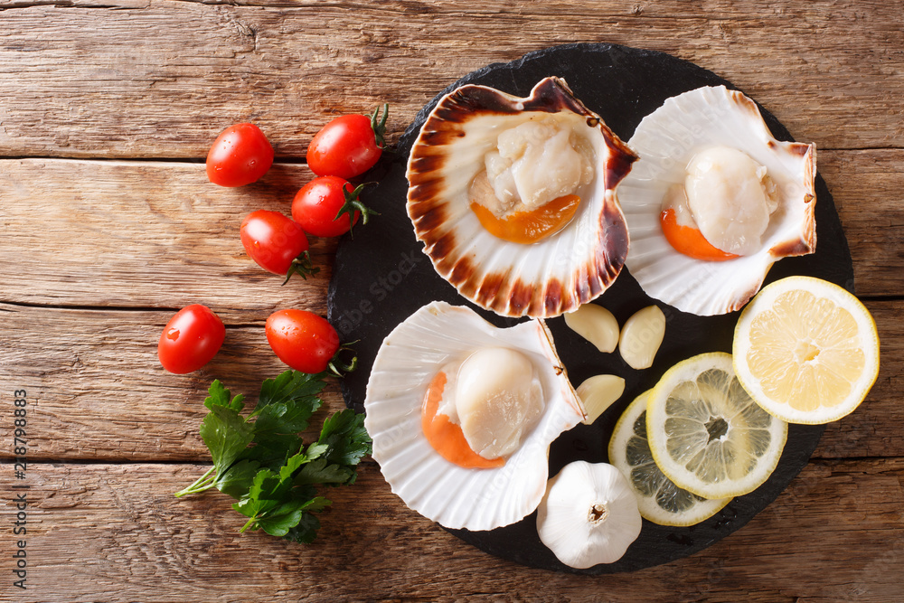 Delicious raw scallops in a shell and tomatoes, garlic, parsley and lemon close-up. Horizontal top view background Delicious raw scallops in a shell and tomatoes, garlic, parsley and lemon close-up. Horizontal top view background