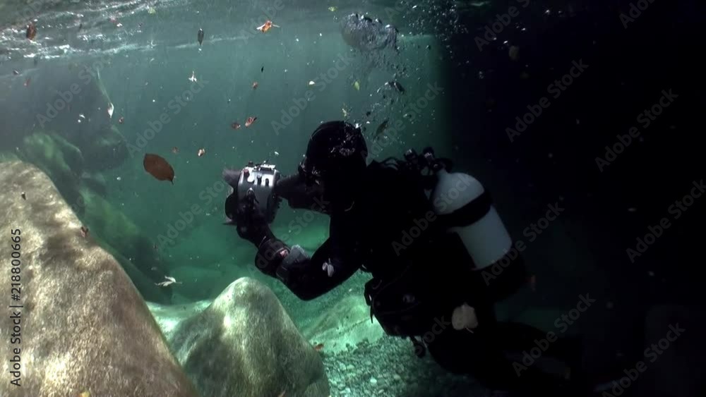 Divers with camera underwater in transparent river Verzasca. Picturesque nature on background of huge smooth stones in canton of Ticino are favorite place for underwater photographers. Divers with camera underwater in transparent river Verzasca. Picturesque nature on background of huge smooth stones in canton of Ticino are favorite place for underwater photographers.