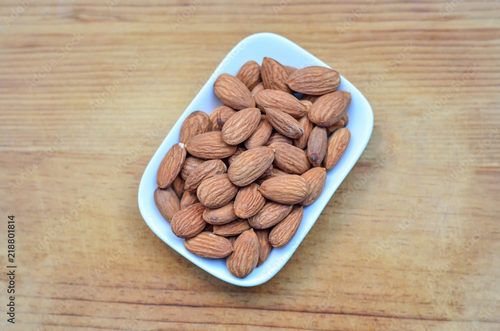 Salted roast organic almonds on a white plate on wood background Salted roast organic almonds on a white plate on wood background
