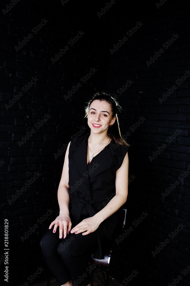 Portrait of a beautiful brunette girl in black jumpsuit sitting and posing in the studio. Portrait of a beautiful brunette girl in black jumpsuit sitting and posing in the studio.