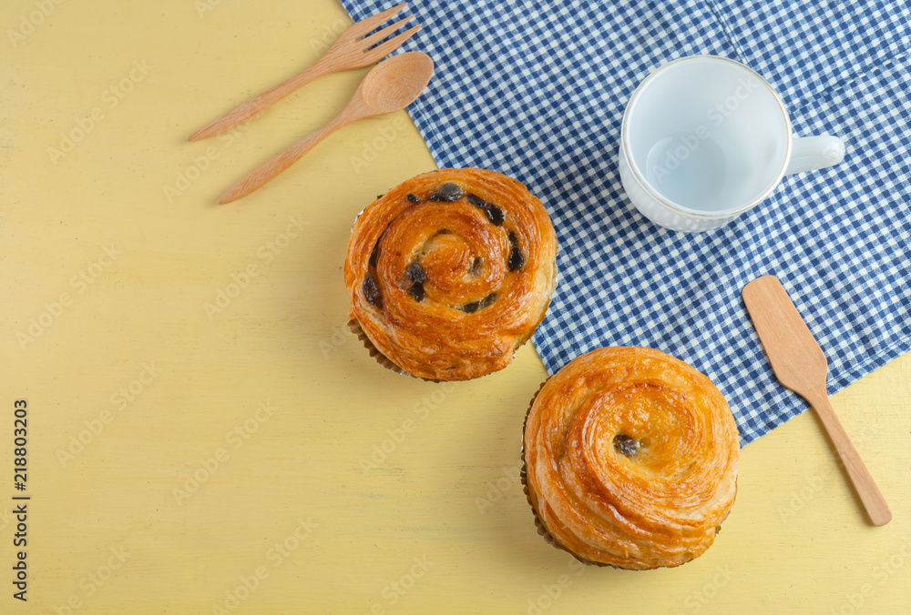 Raisin danish pastry on the yellow wood and blue gingham check cloth. Colourful tasty sweet bakery..