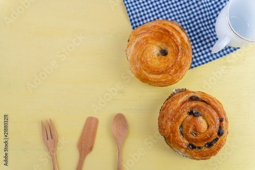 Raisin danish pastry on the yellow wood and blue gingham check cloth. Colourful tasty sweet bakery..
