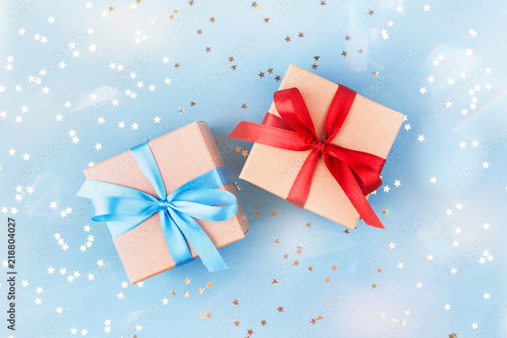 Two gift boxes wrapped in kraft paper and tied with ribbon on blue background decorated with confetti. Top view, gift idea for him and her. Two gift boxes wrapped in kraft paper and tied with ribbon on blue background decorated with confetti. Top view, gift idea for him and her.