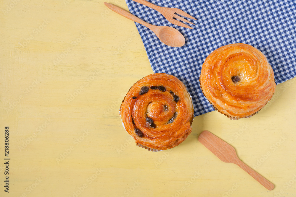 Raisin danish pastry on the yellow wood and blue gingham check cloth. Colourful tasty sweet bakery..