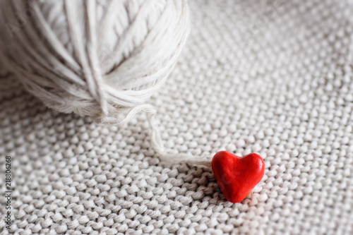 red heart and a ball of threads on a knitted background close-up