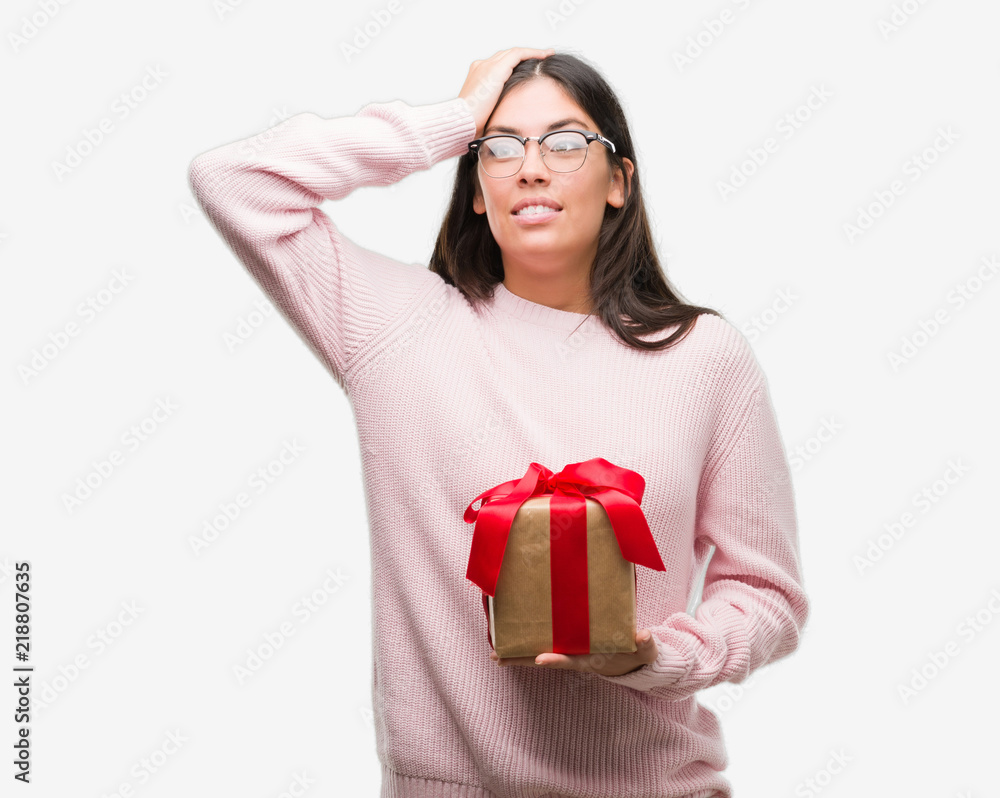 Young hispanic woman holding a gift stressed with hand on head, shocked with shame and surprise face, angry and frustrated. Fear and upset for mistake. Young hispanic woman holding a gift stressed with hand on head, shocked with shame and surprise face, angry and frustrated. Fear and upset for mistake.